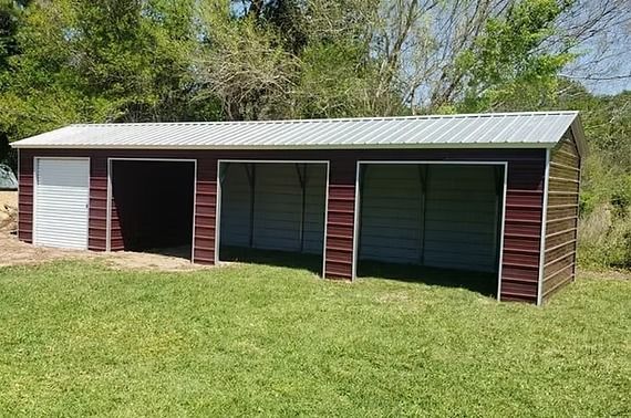 A metal garage with three doors is sitting in the middle of a lush green field.