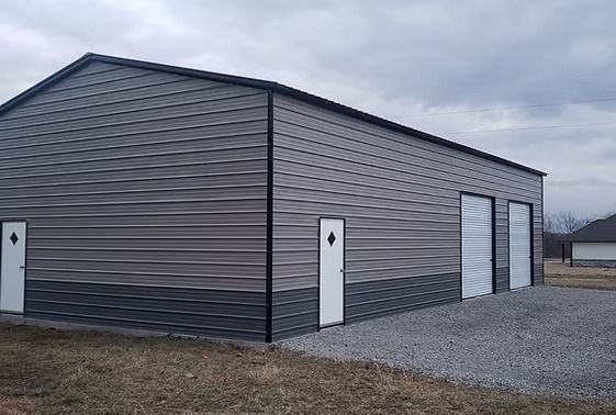 A large metal building with three doors is sitting in the middle of a grassy field.