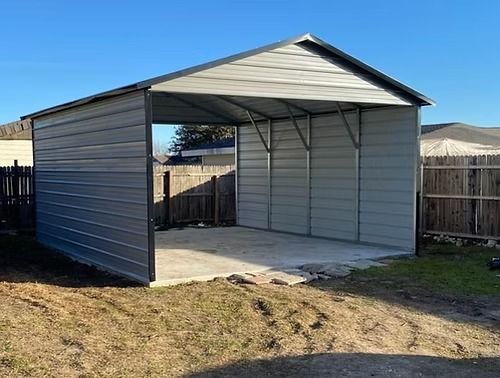 A metal garage with a concrete floor is in the backyard of a house.