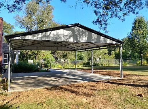 A carport is sitting in the middle of a driveway next to a house.