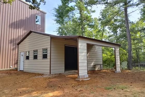 A metal garage with a porch is sitting in the dirt in front of a building.