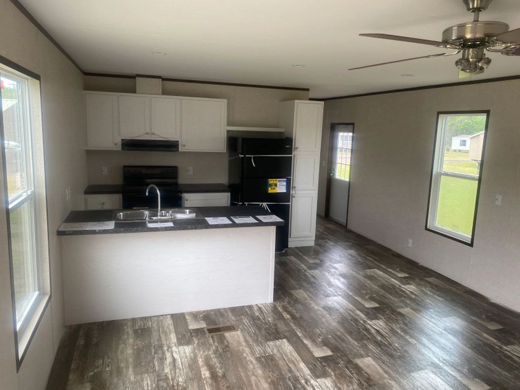 A kitchen and living room in a mobile home with a ceiling fan.