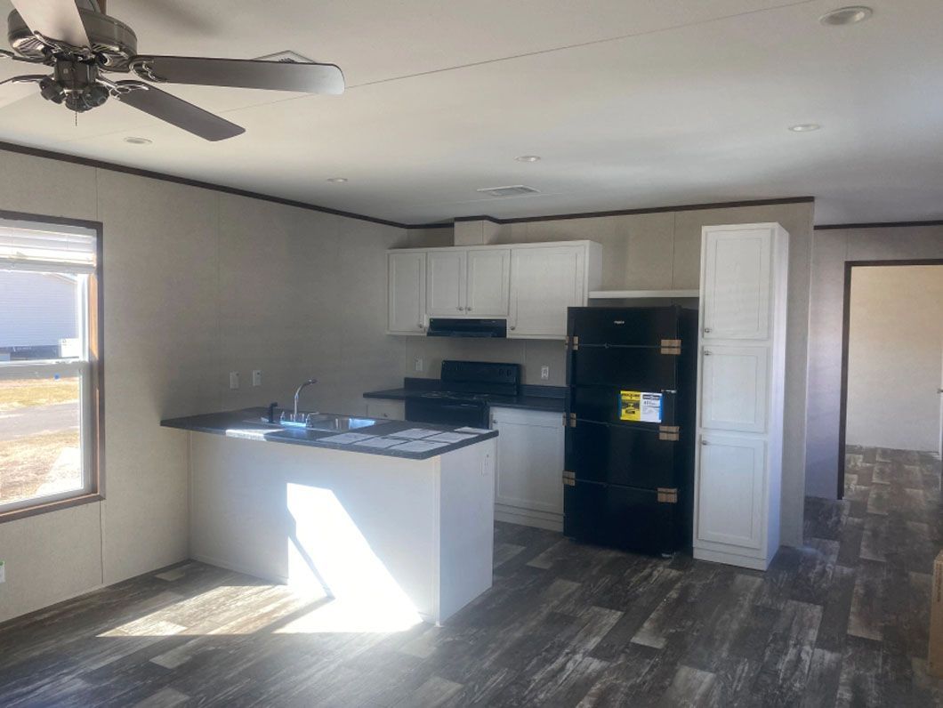 A kitchen in a mobile home with a ceiling fan and a refrigerator.