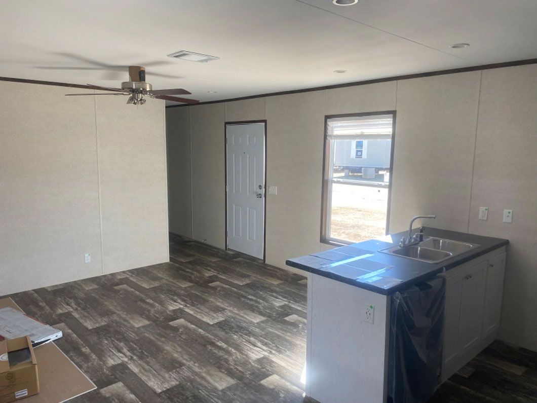 A living room with a ceiling fan and a sink in a mobile home.