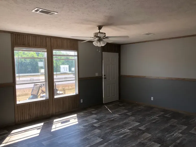 An empty living room with a ceiling fan and two windows.