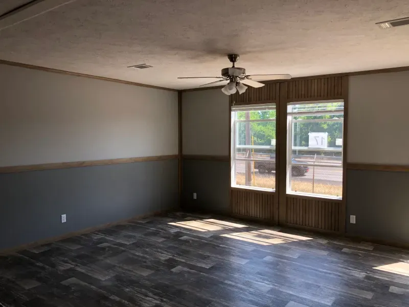 An empty living room with a ceiling fan and two windows.
