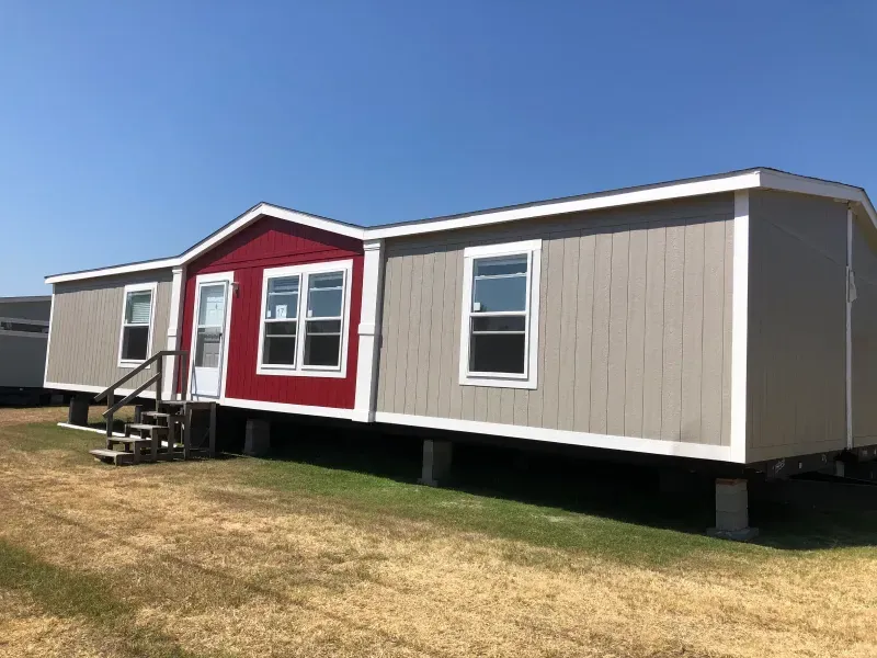 A mobile home with a red roof is sitting on top of a lush green field.