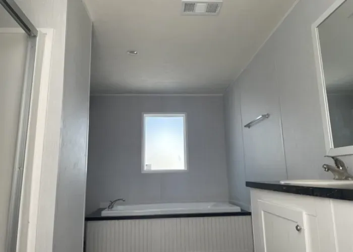 A bathroom with a tub , sink , mirror and window.