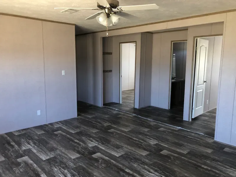 An empty room with a ceiling fan and a wooden floor.