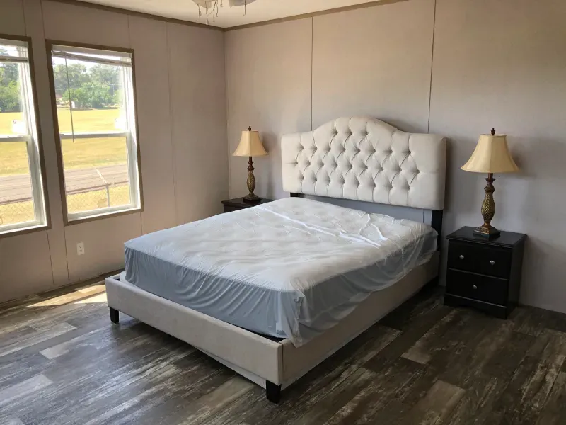 A bedroom with a bed , two lamps , and two windows.