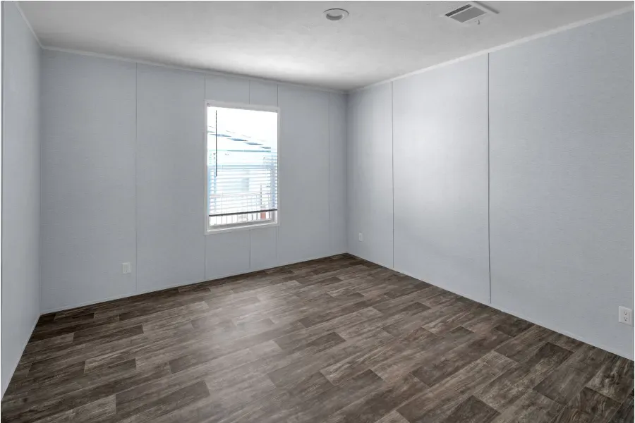 An empty room with a window and wooden floors.