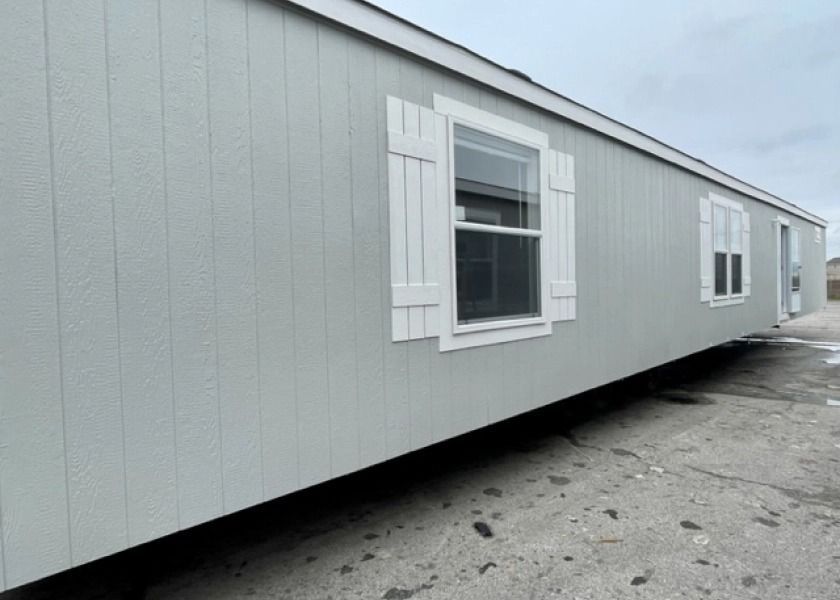 A mobile home with white shutters on the windows is parked on the side of the road.