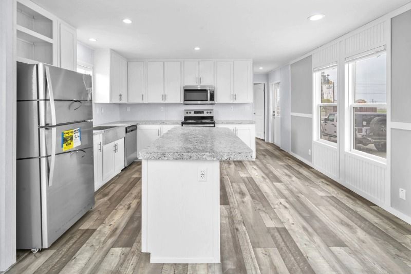 A kitchen with white cabinets , stainless steel appliances , hardwood floors and a large island.