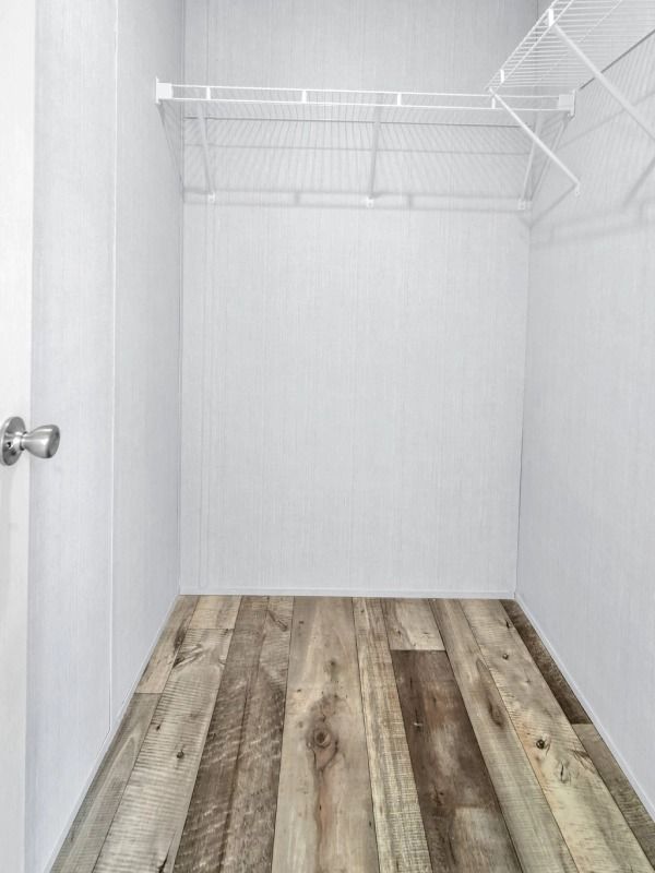 An empty walk in closet with wooden floors and shelves.