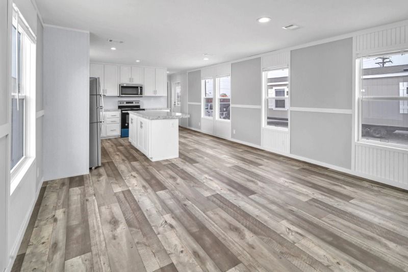 A large empty room with hardwood floors and a kitchen.