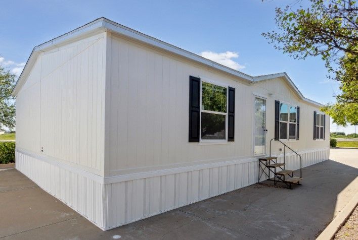 A white mobile home with black shutters and stairs.