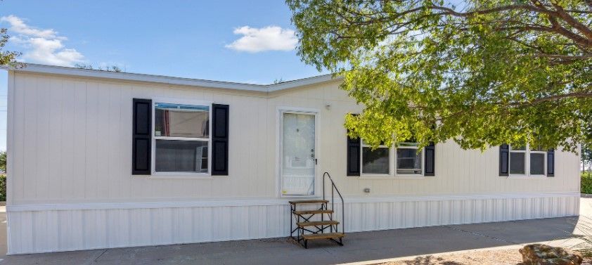 A white mobile home with black shutters and stairs.