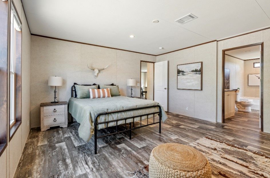 A bedroom with a bed , nightstands , lamps and a wicker ottoman.