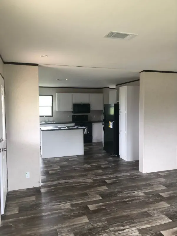 An empty room with a wooden floor and a kitchen in the background.