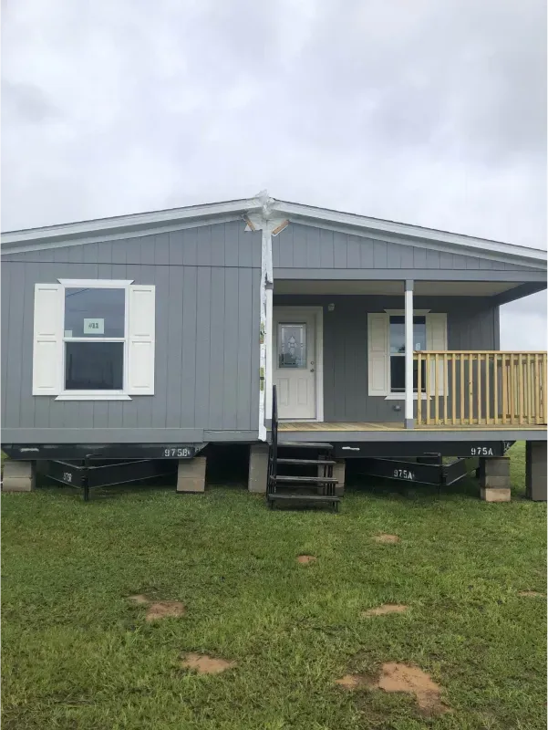 A mobile home with a porch and stairs in a grassy field.