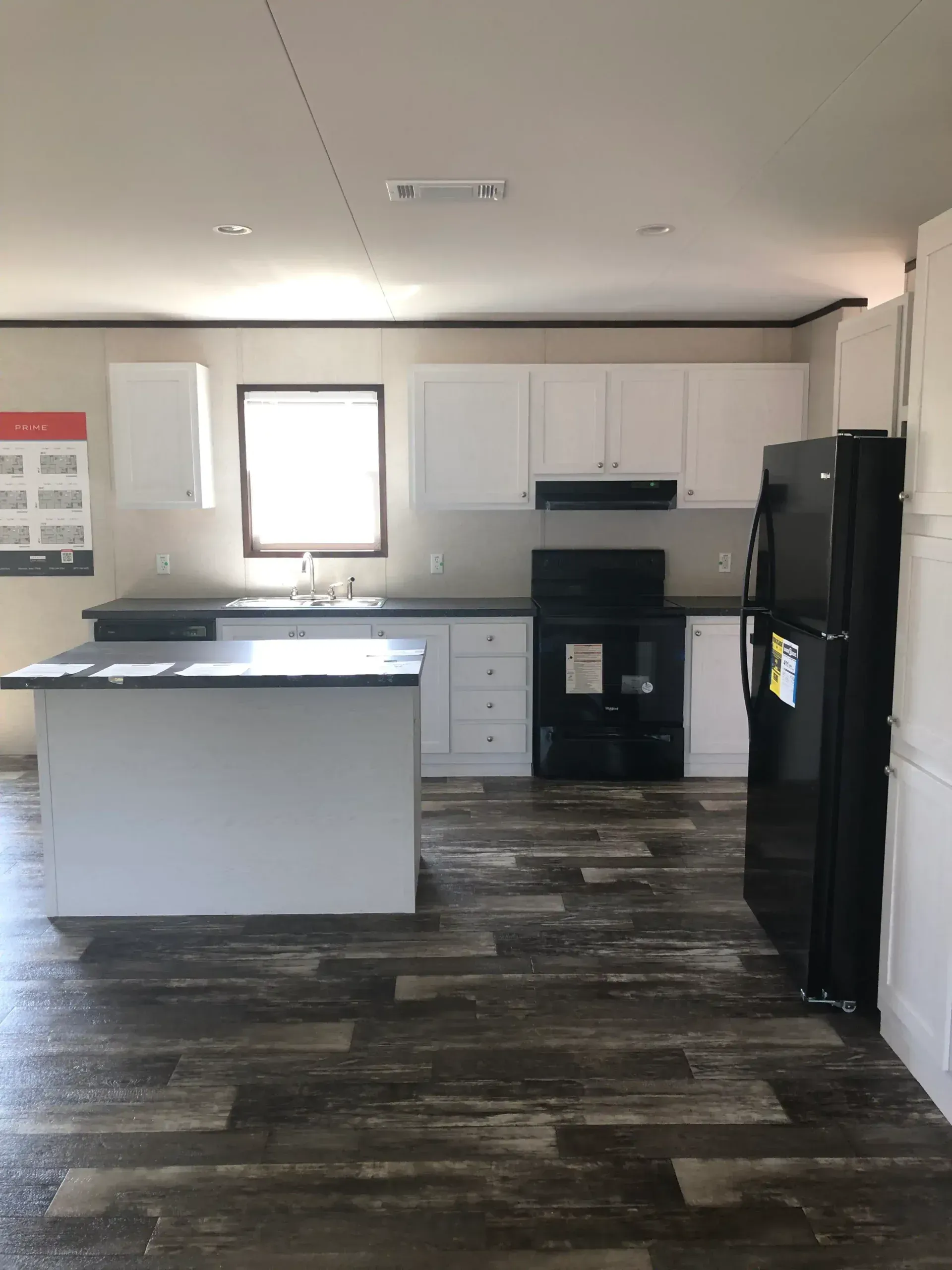 A kitchen with white cabinets , a black refrigerator , a stove and a sink.