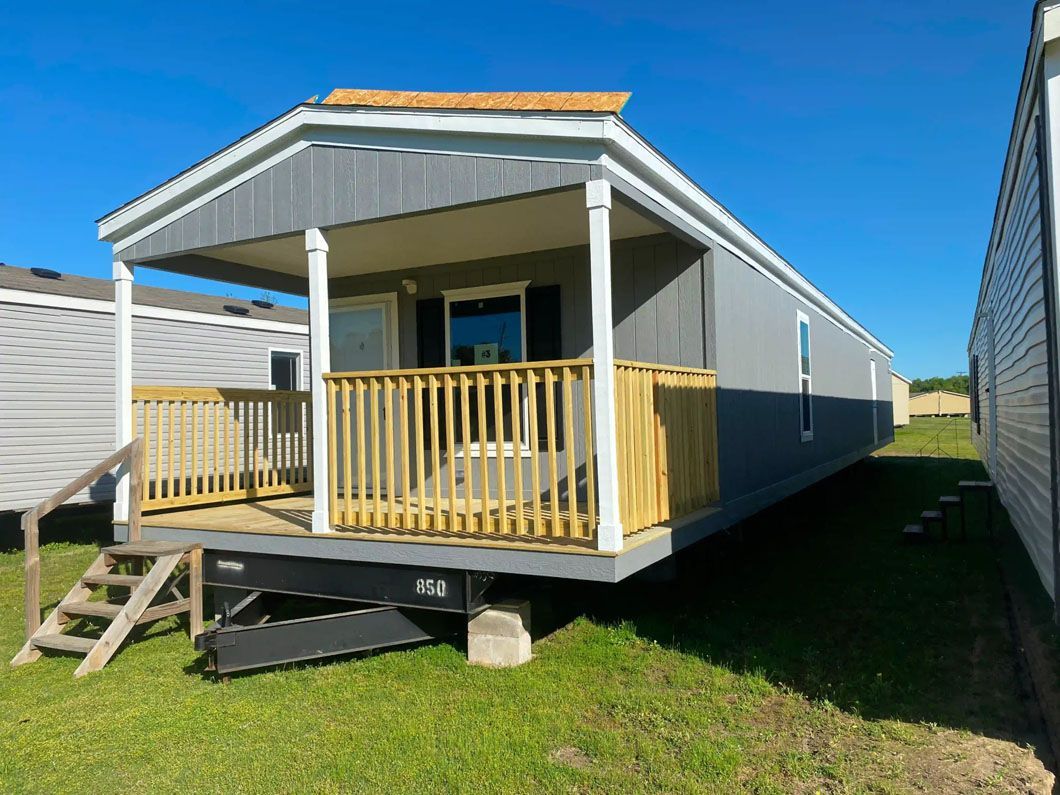 A mobile home with a porch and stairs is sitting on top of a lush green field.