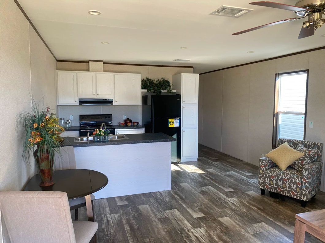 A living room with a table and chairs and a kitchen with a ceiling fan.