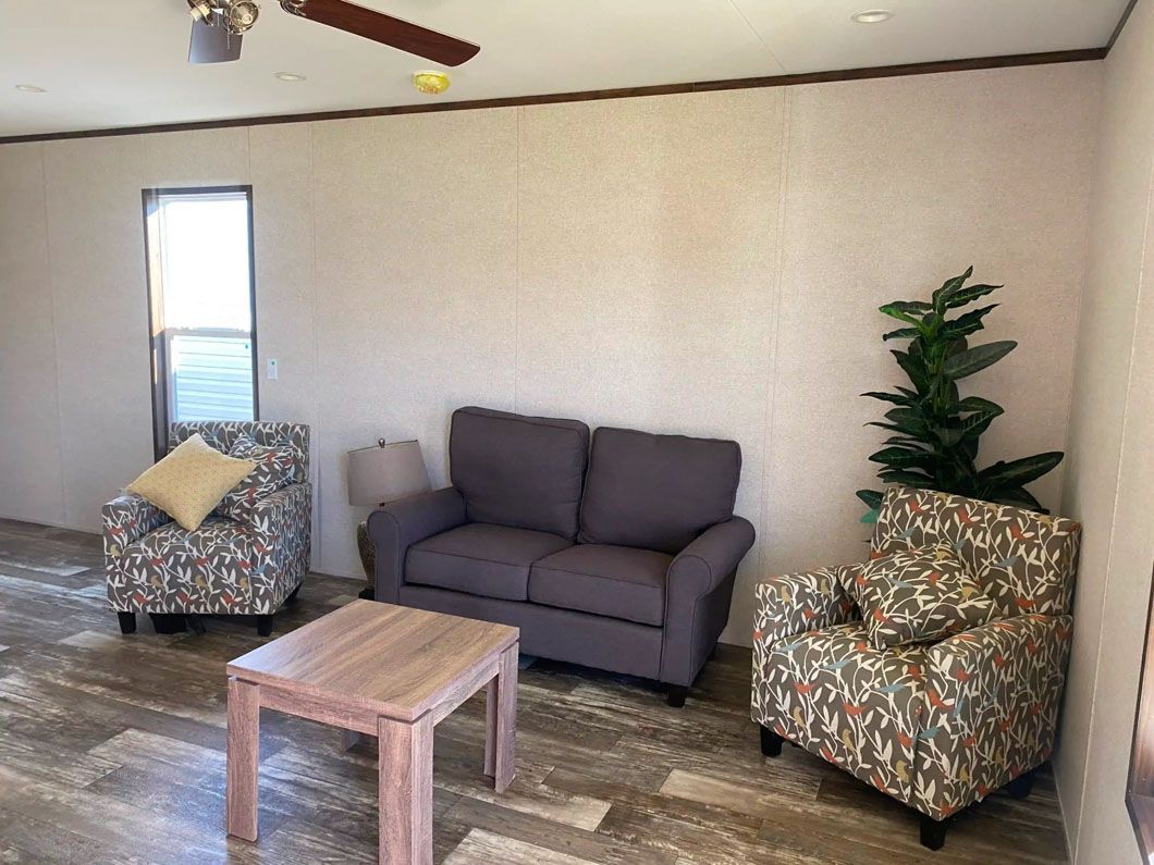 A living room with a couch , two chairs , a table and a ceiling fan.