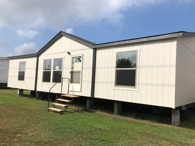 A mobile home with stairs leading up to it is sitting on top of a lush green field.