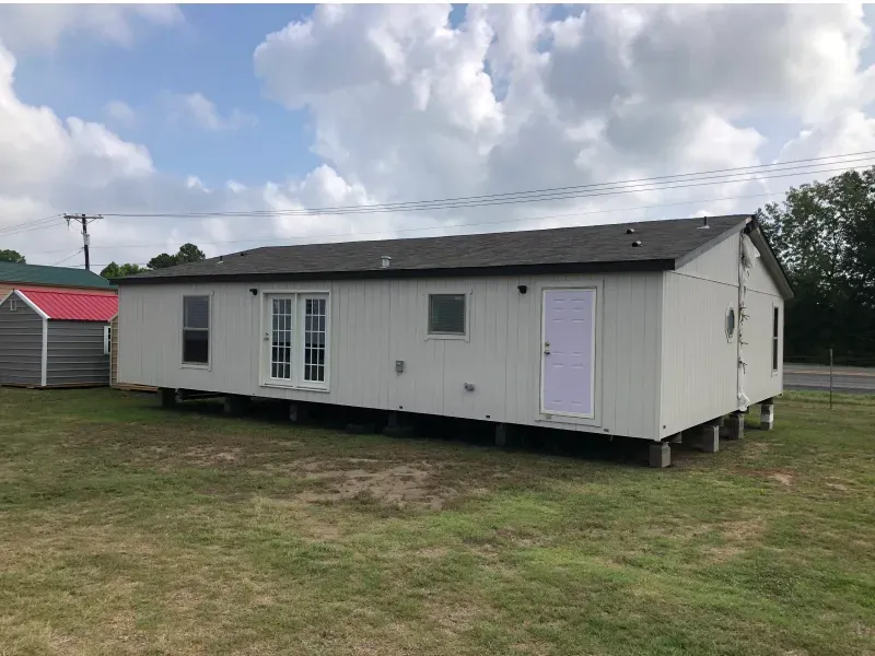 A mobile home is parked in a grassy field next to a shed.