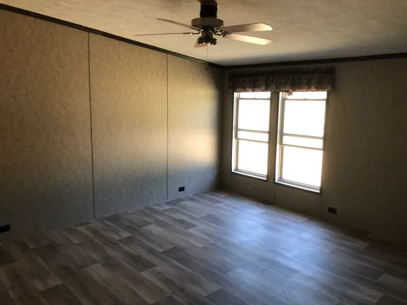 An empty room with a ceiling fan and two windows
