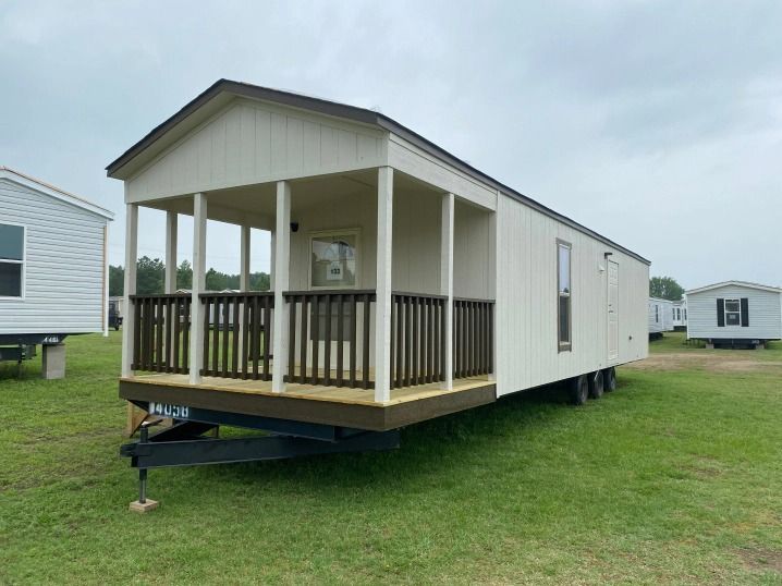 A mobile home with a porch is parked in a grassy field.