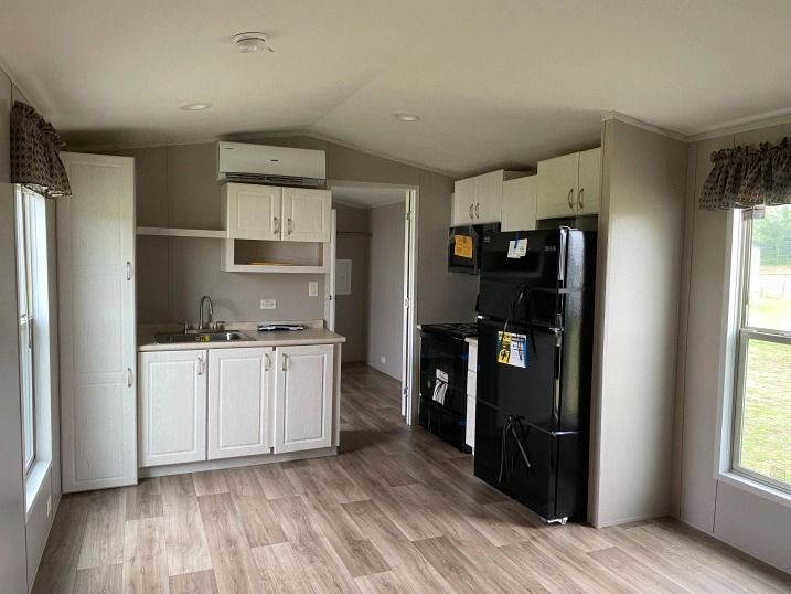 A kitchen in a mobile home with white cabinets and a black refrigerator.