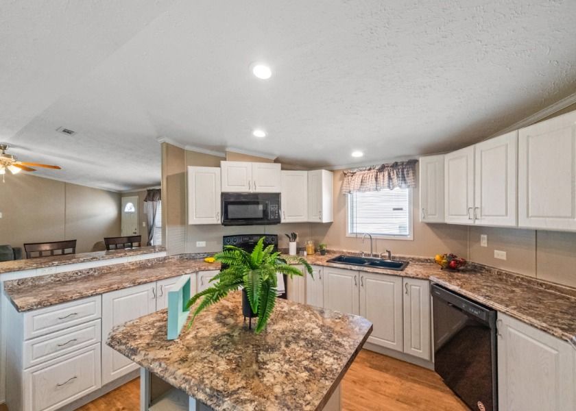 A kitchen in a mobile home with white cabinets and granite counter tops.