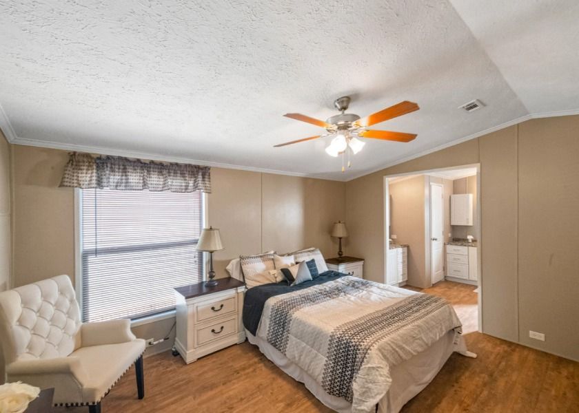 A bedroom with a bed , chair , nightstand and ceiling fan.