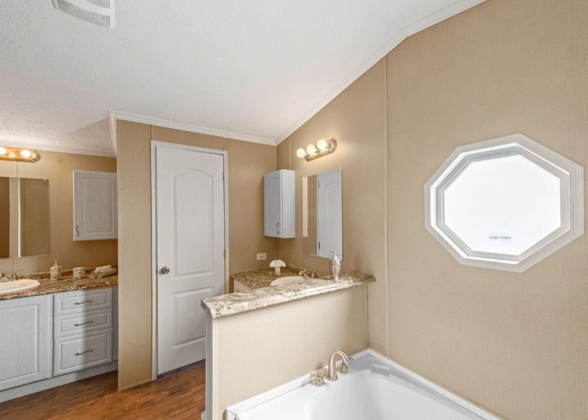 A bathroom with two sinks , a tub , a mirror and a window.