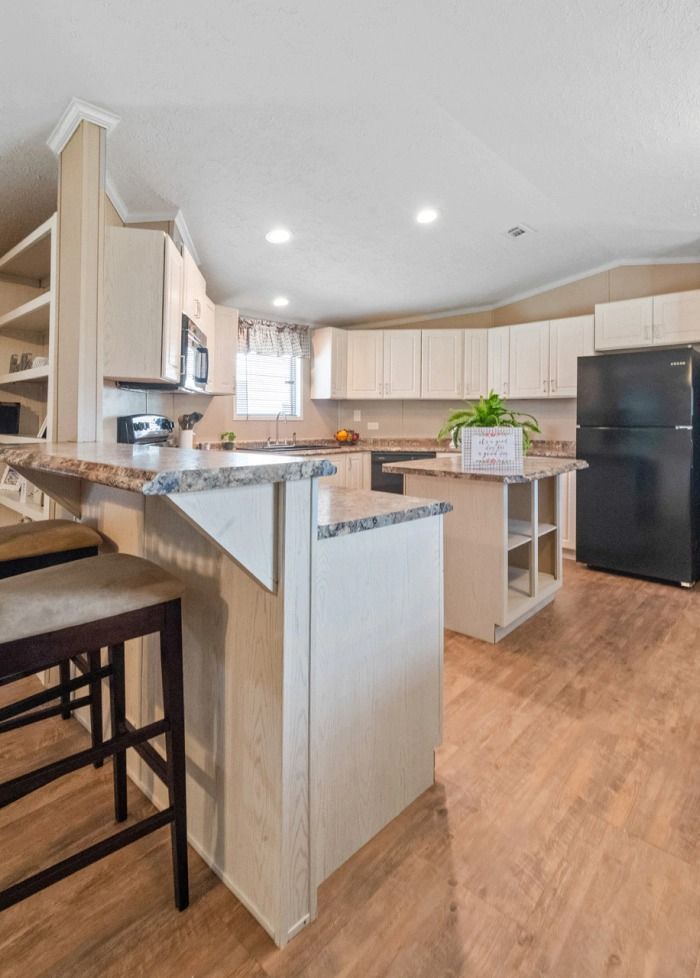 A kitchen with a black refrigerator , white cabinets , and wooden floors.