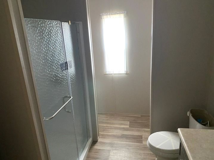 A bathroom with a toilet , shower and window.