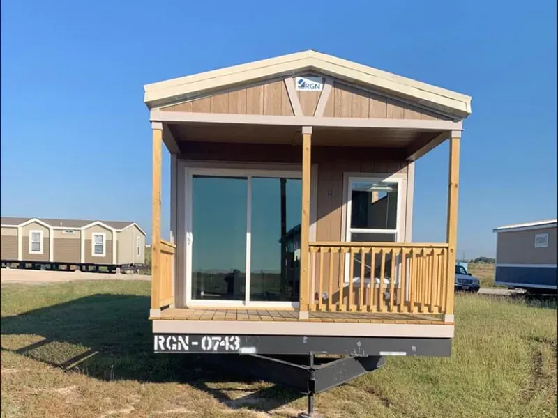 A small house with a porch and sliding glass doors is parked in a field.