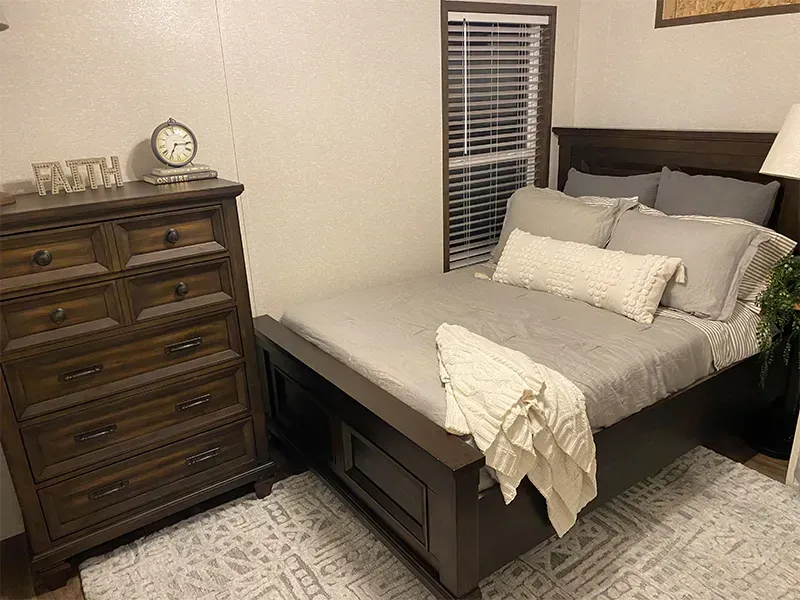 A bedroom with a bed , dresser , lamp and window.