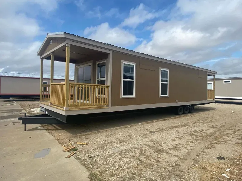 A mobile home with a porch is parked in a dirt lot.