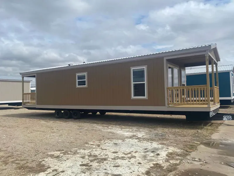 A mobile home with a porch is parked in a dirt field.