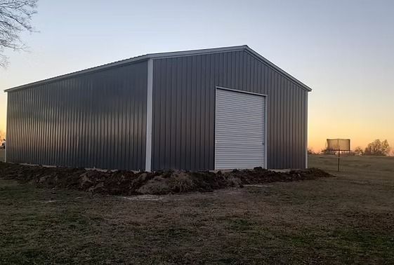 A metal building with a white door is sitting in the middle of a grassy field.