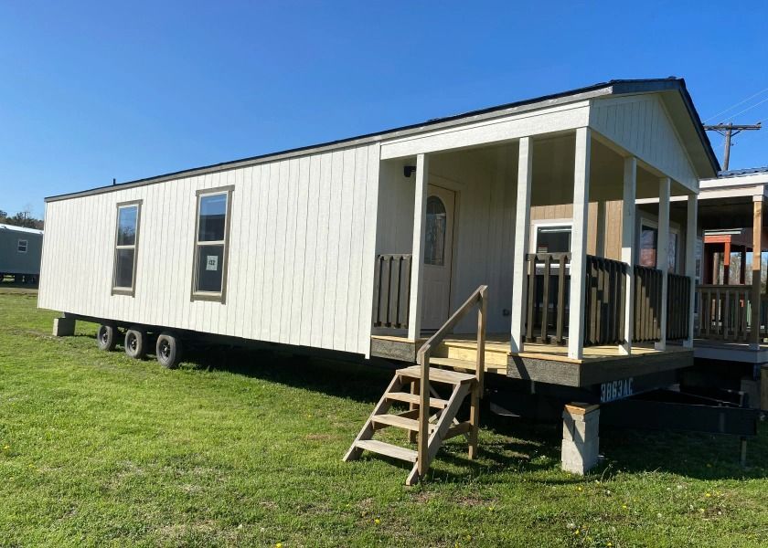 A mobile home with a porch and stairs is parked in a grassy field.