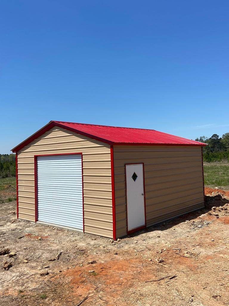 A small metal garage with a red roof is sitting in the middle of a dirt field.