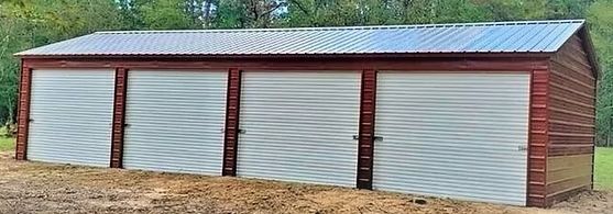 A garage with three doors and a metal roof is sitting in the middle of a field.