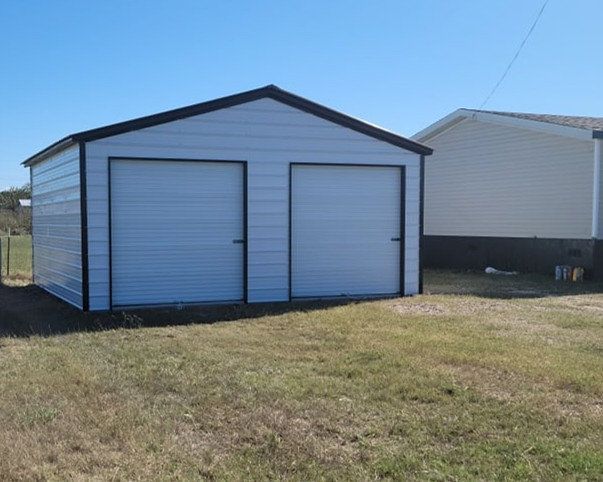 A white garage with two doors is sitting in the middle of a grassy field.