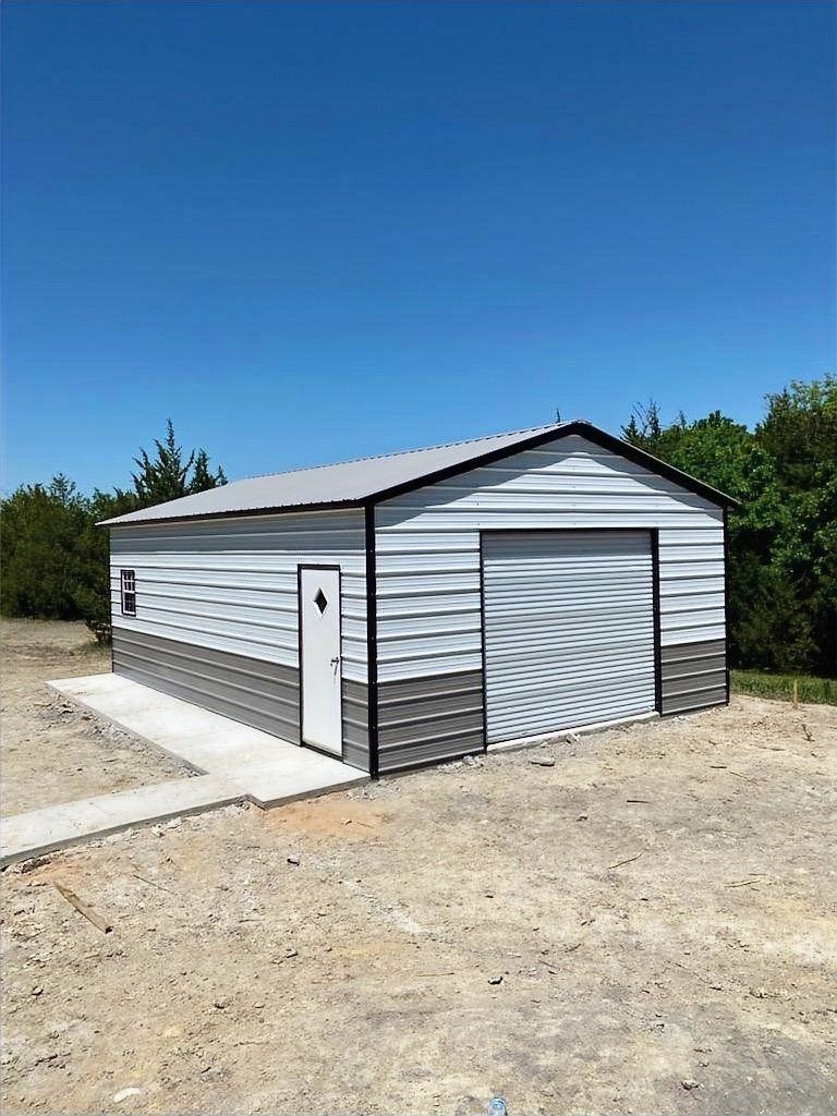 A metal garage with a concrete walkway leading to it is sitting in the middle of a dirt field.