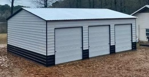 A white garage with three garage doors is sitting on top of a dirt field.