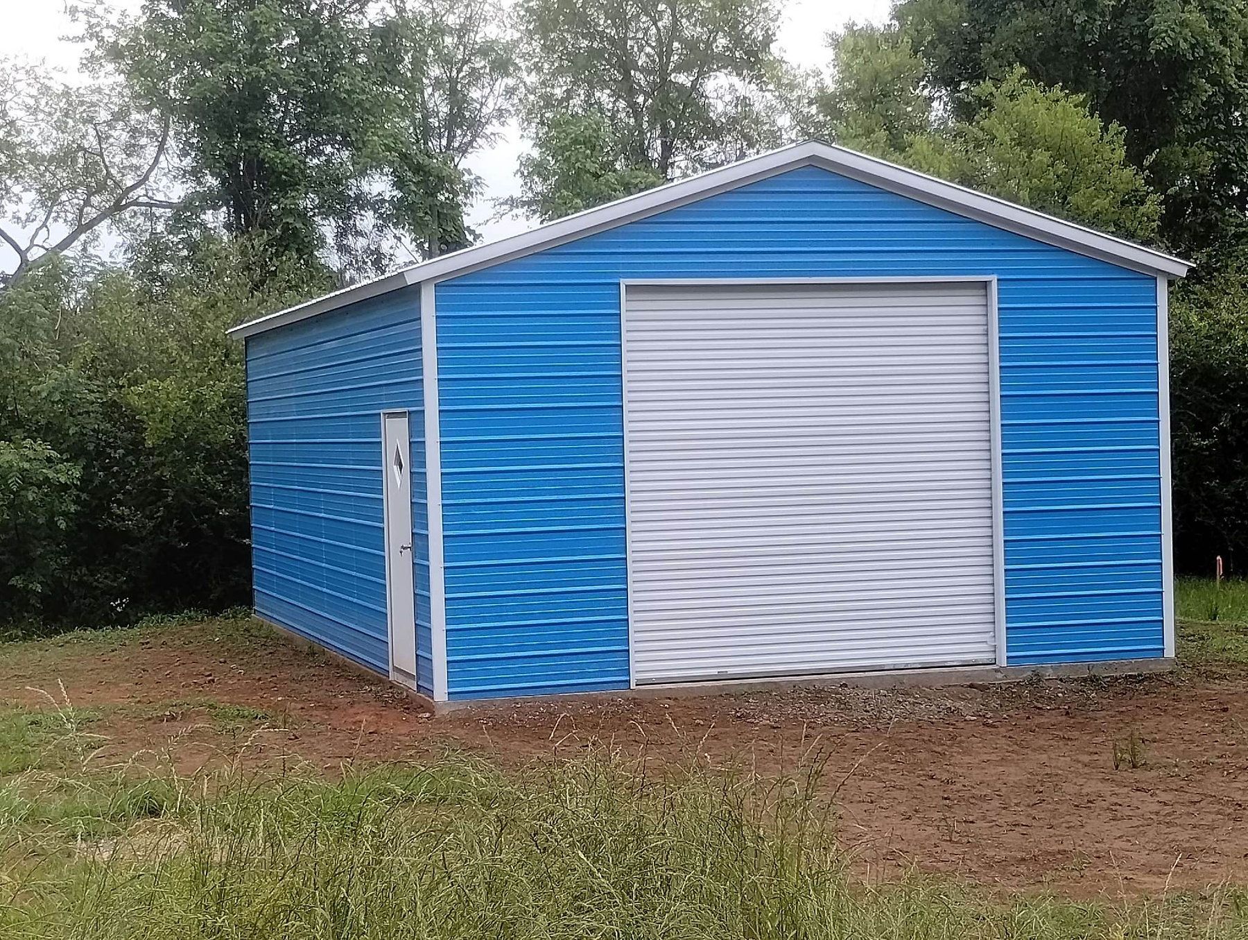 A blue garage with a white garage door is sitting in the middle of a grassy field.